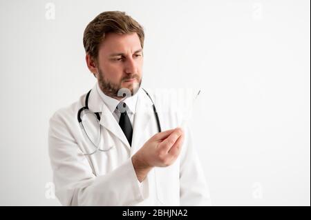 Portrait du médecin mâle avec stéthoscope en uniforme médical est en regardant le thermomètre se posant sur un fond blanc isolé Banque D'Images