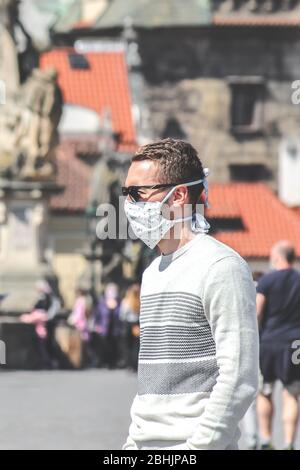 Jeune homme avec lunettes de soleil et masque en tissu cousu photographié sur le pont Charles à Prague, en République tchèque. Brouillé dans l'arrière-plan. Voyager, tourisme pendant coronavirus. COVID-19. Banque D'Images