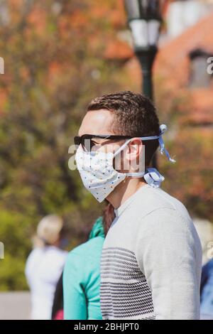 Jeune homme avec lunettes de soleil et masque en tissu cousu photographié sur le pont Charles à Prague, en République tchèque. Brouillé dans l'arrière-plan. Voyager, tourisme pendant coronavirus. COVID-19. Banque D'Images