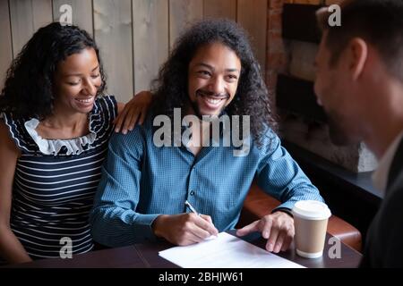 Un couple multiracial heureux signe un accord de clôture de document dans le café Banque D'Images