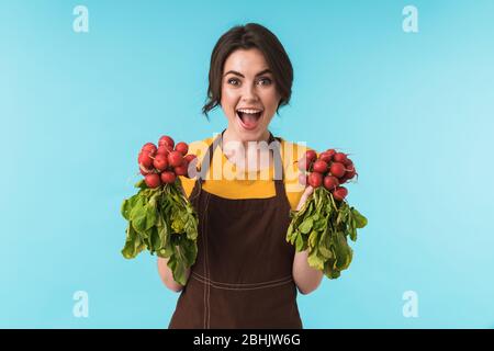 Image de la jeune femme chef enchantée et charmante, avec un radish isolé sur fond de mur bleu. Banque D'Images