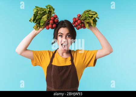 Image de la jeune femme chef enchantée et charmante, avec un radish isolé sur fond de mur bleu. Banque D'Images