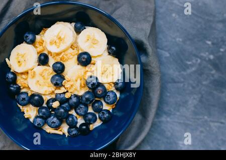 Gros plan bol bleu foncé de gruau de porridge avec banane et bleuet sur la vue vintage de table dans le style plat. Petit déjeuner chaud et cuisine maison Banque D'Images