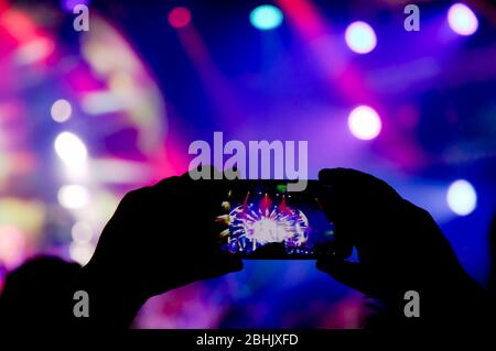 La collecte de mémoire numérique perd la capacité d'être présent, la silhouette d'une personne qui prend des effets de lumière sur la scène de concert avec un smartphone Banque D'Images