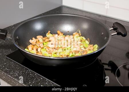 Champignons frits champagnes, poireaux verts, cuillère en bois dans la poêle à frire près Banque D'Images