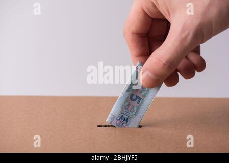 Concept de don d'argent. Cadrer gros plan photo de la main masculine mettant l'argent ukrainien plié dans la boîte en carton Banque D'Images