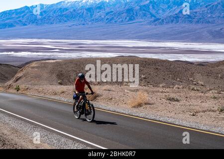 Un cycliste solitaire persévère sur la montée le long de la promenade Artist's Palette dans le parc national de la Vallée de la mort Banque D'Images