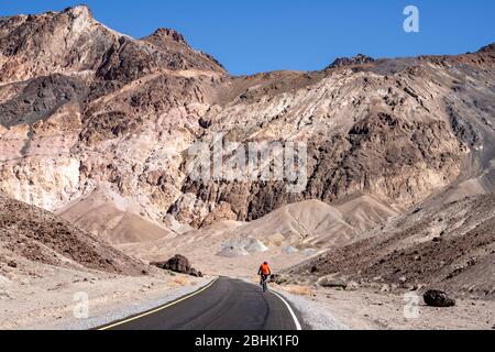 Un cycliste solitaire persévère sur la montée le long de la promenade Artist's Palette dans le parc national de la Vallée de la mort Banque D'Images