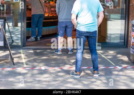 Bande adhésive placée sur le sol pour s'assurer que les gens sont éloignés les uns des autres. Distanciation sociale des personnes en attente en ligne file devant un magasin de nourriture Banque D'Images