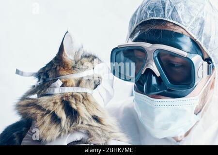 Médecin de l'homme dans des lunettes de protection avec les bras croisés et le chaton de chat est sûr du coronavirus dans le masque de protection médicale. Pandémie mondiale Banque D'Images