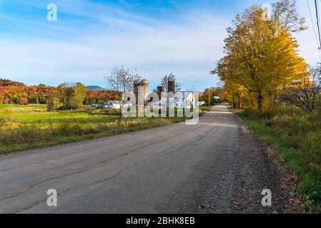 Paysage rural avec une ferme le long d'une route arrière vide sur une journée d'automne claire. Des couleurs d'automne époustouflantes. Banque D'Images