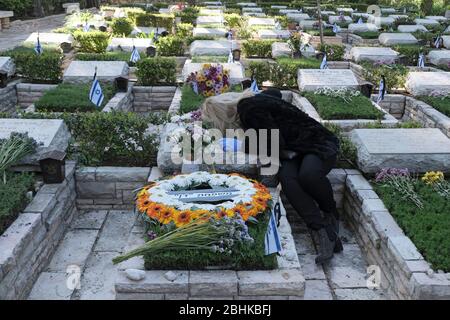 Jérusalem, Israël. 26 avril 2020. Une femme israélienne grime sur la tombe d'un être cher à l'armée nationale du Mont-Herzl à Jérusalem alors qu'Israël se prépare à marquer le jour du souvenir des soldats tombés. Les cérémonies officielles ne se dérouleront pas cette année en raison d'un couvre-feu national pour lutter contre la pandémie COVID-19. Banque D'Images