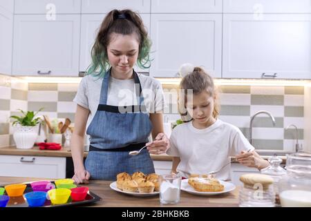 Enfants deux sœurs filles préparant des muffins dans la cuisine maison. Les enfants saupoudrer décorant des gâteaux faits maison fraîchement cuits avec de la poudre de sucre blanc Banque D'Images