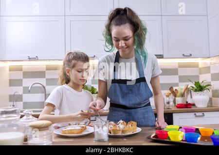 Enfants deux sœurs filles préparant des muffins dans la cuisine maison. Les enfants saupoudrer décorant des gâteaux faits maison fraîchement cuits avec de la poudre de sucre blanc Banque D'Images