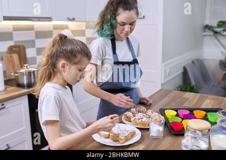 Enfants deux sœurs filles préparant des muffins dans la cuisine maison. Les enfants saupoudrer décorant des gâteaux faits maison fraîchement cuits avec de la poudre de sucre blanc Banque D'Images