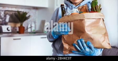 Une personne souriant pour l'appareil photo avec un ensemble de nourriture dans la main. Sac en papier avec fournitures alimentaires crise stock alimentaire pour la période d'isolement de quarantaine. Livraison de nourriture, don, coronavirus. Mise au point douce. Banque D'Images