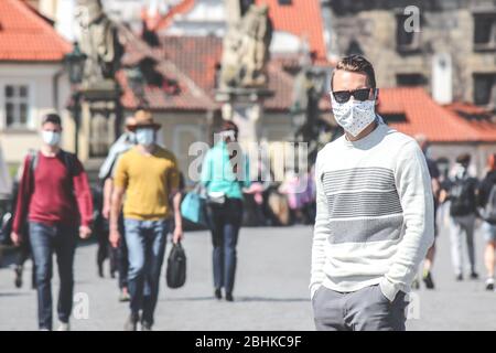 Jeune homme avec lunettes de soleil et masque en tissu cousu photographié sur le pont Charles à Prague, en République tchèque. Brouillé dans l'arrière-plan. Voyager, tourisme pendant coronavirus. COVID-19. Banque D'Images