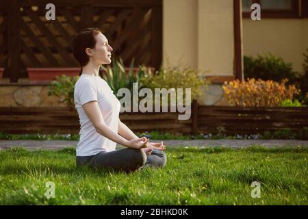 Une jeune femme méditant sur l'herbe dans la cour près de la maison. Banque D'Images