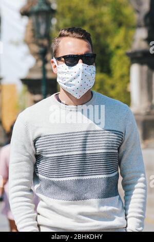 Jeune homme avec lunettes de soleil et masque en tissu cousu photographié sur le pont Charles à Prague, en République tchèque. Arrière-plan flou. Voyager, tourisme pendant coronavirus. COVID-19. Photo verticale. Banque D'Images