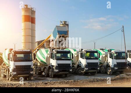 Rangée de nombreux grands mélangeurs modernes stationnés contre l'usine mobile temporaire de béton sur le nouveau chantier de construction de routes asphaltées le matin. Lourd Banque D'Images