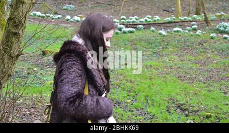 Profil de la femme de brunette à poil long marchant dans une forêt d'hiver: Sol boueux et fleurs blanches de neige en arrière-plan Banque D'Images
