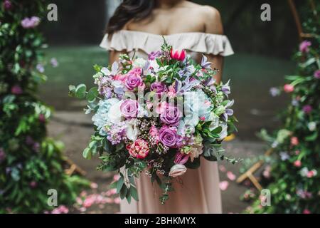 Mariée tenant dans les mains incroyable énorme bouquet fleuri sur la cérémonie de mariage. Roses roses roses, pivoines, tulipes rouges et greens se rapprochés. Banque D'Images