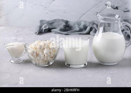 Produits laitiers: Lait, kéfir ou ayran, fromage cottage et crème aigre dans un bol transparent, pichet et verre sur un fond gris, gros plan Banque D'Images