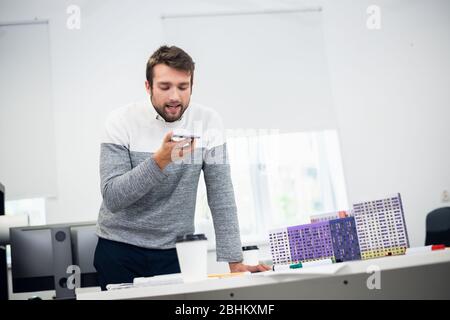 Portrait d'un jeune architecte parlant à quelqu'un par téléphone en utilisant le mode haut-parleur. Banque D'Images
