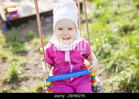 Bonne petite fille sur des balançoires dans le jardin de printemps. Jolie fille regardant l'appareil photo et souriant. Banque D'Images