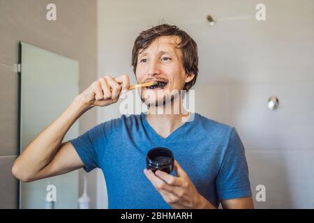 Les dents de jeune homme se brossent à l'aide de poudre De charbon Activée pour brosser et blanchir les dents. Brosse écologique en bambou Banque D'Images