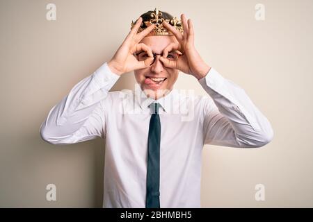 Jeune homme d'affaires caucasien portant la couronne dorée sur un arrière-plan isolé faisant bon geste comme des jumelles qui s'écarent de la langue, yeux regardant Banque D'Images