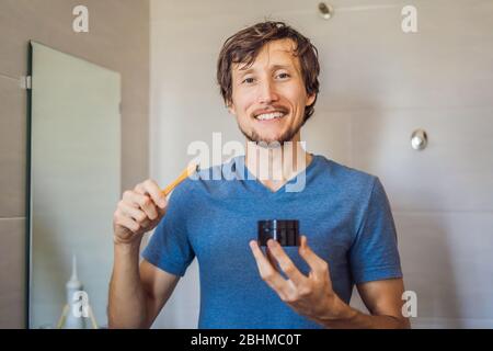 Les dents de jeune homme se brossent à l'aide de poudre De charbon Activée pour brosser et blanchir les dents. Brosse écologique en bambou Banque D'Images