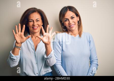 Couple de sœurs d'âge moyen se tenant sur un fond blanc isolé montrant et pointant vers le haut avec les doigts numéro dix tout en souriant confiant Banque D'Images