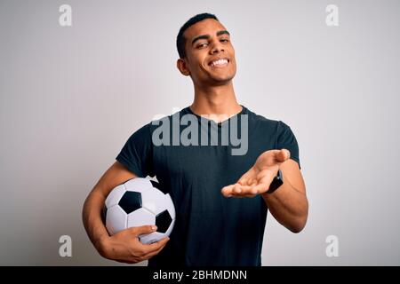 Bel homme africain américain jouant à la base de football tenant le ballon de football sur fond blanc souriant offrant main de paume donnant l'aide et l'acce Banque D'Images