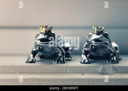 Deux figurines couronnées de prince grenouille en argent sterling assis dans le seuil de vent, concept de couleur. Banque D'Images