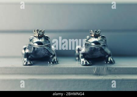 Deux figurines couronnées de prince grenouille en argent sterling assis dans le seuil de vent, concept de couleur. Banque D'Images