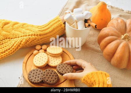 Latte de citrouille dans les mains féminines. Femme boit du café avec épices et biscuits d'automne saisonniers. Banque D'Images