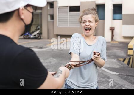 Une jeune femme blanche effrayée est volée de mugged par l'homme masqué. Concept d'attaque de vol de rue Banque D'Images