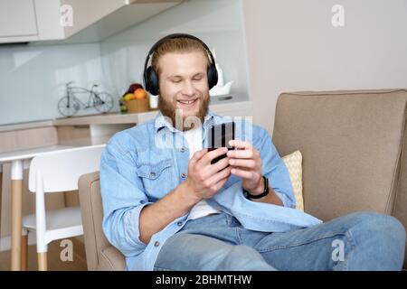 Un jeune homme heureux portant un casque à l'aide du téléphone détendez-vous sur le canapé. Banque D'Images