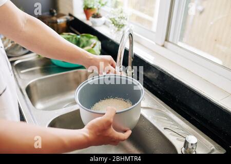 Femme rinçant la cuvette de riz sous l'eau du robinet dans la cuisine lors de la cuisson du dîner à la maison Banque D'Images