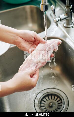 Femme rinçant une partie de bacon sous l'eau du robinet avant de cuisiner le petit déjeuner à la maison Banque D'Images