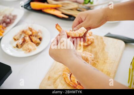 Image rapprochée de la femme qui expluche des crevettes bouillies lors de la préparation d'une salade saine pour le déjeuner Banque D'Images