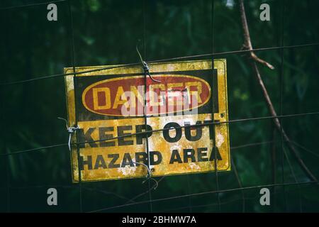 Signe de danger avec texte GARDER HORS DE LA ZONE DE DANGER comme message d'avertissement suspendu sur la zone sombre clôturée, affiche sale à l'extérieur. Banque D'Images