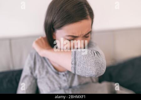 COVID-19 toux Coronavirus réduction du risque de propagation de l'infection en couvrant le nez et la bouche lors de la toux et des éternuements avec un coude fléchi. Jeune fille à la toux à la maison dans la prévention des bras. Banque D'Images