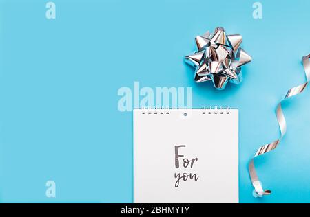 cahier sur une spirale avec feuilles blanches et lettres noires pour vous et un fond bleu avec un noeud en feuille d'argent et des rubans argentés Banque D'Images