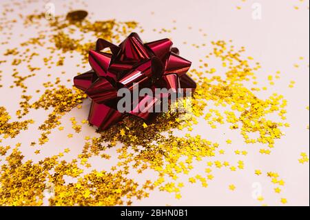 grand noeud en feuille rouge sur fond d'étoiles d'or éparses sur un fond beige doux. Banque D'Images