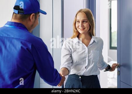 Souriant belle jeune femme ouvrant la porte d'entrée et saluant réparateur Banque D'Images