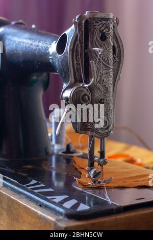 Ancienne machine à coudre rétro et tissu orange prêt à coudre. Le pied du compresseur est abaissé. Profondeur de champ peu profonde. Concentrez-vous sur le pied du compresseur. Vertical. Banque D'Images
