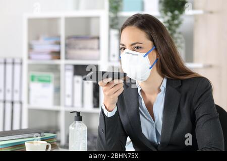 Femme de direction avec masque de protection utilisant le système de reconnaissance vocale sur smartphone au bureau Banque D'Images