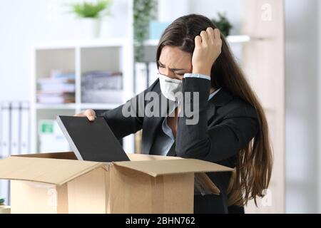 Triste femme exécutive au feu avec masque de protection pour l'emballage des effets personnels sur une boîte au bureau Banque D'Images